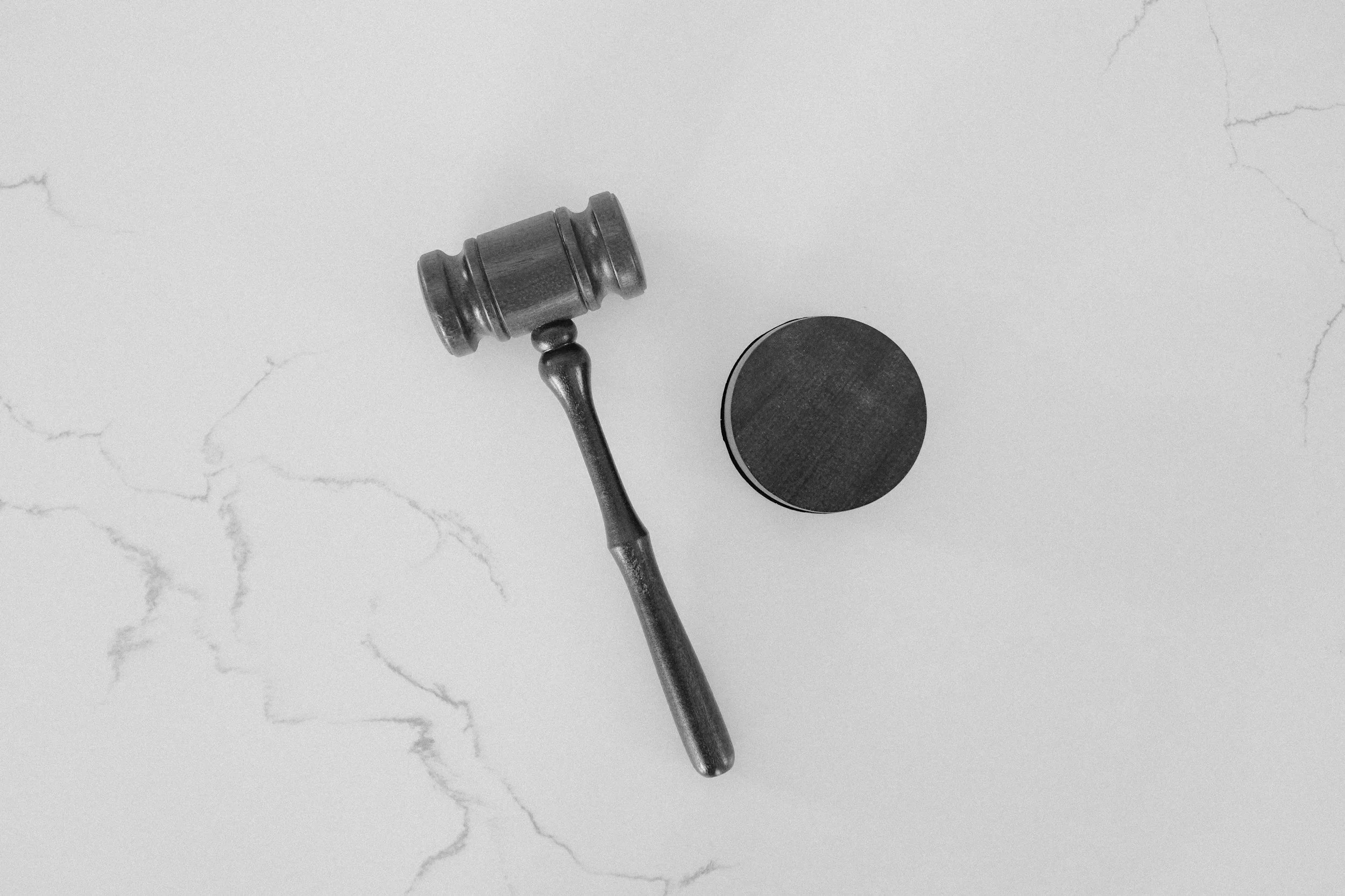 A black gavel resting on a flat surface with a round sound block nearby, seen from above.