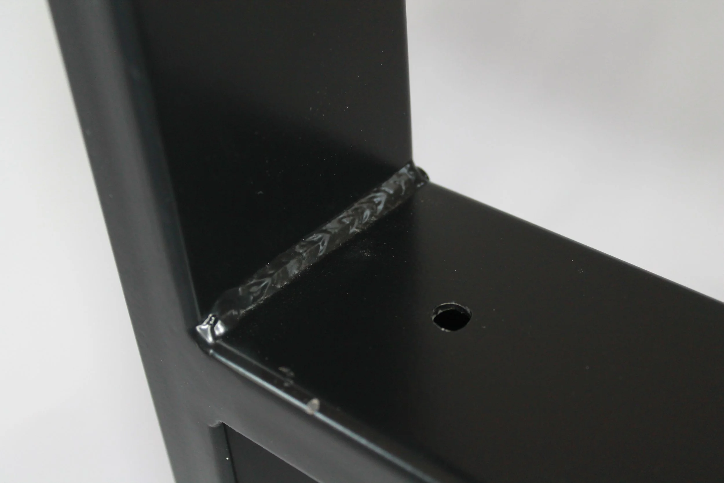 Close-up of a black metal object with a welded joint and a small hole.