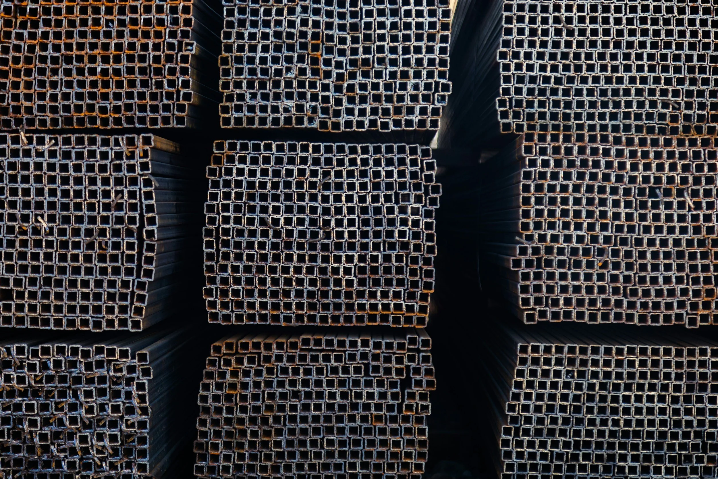 Stacks of metal square tubing arranged in a grid pattern, viewed from above in an industrial setting.