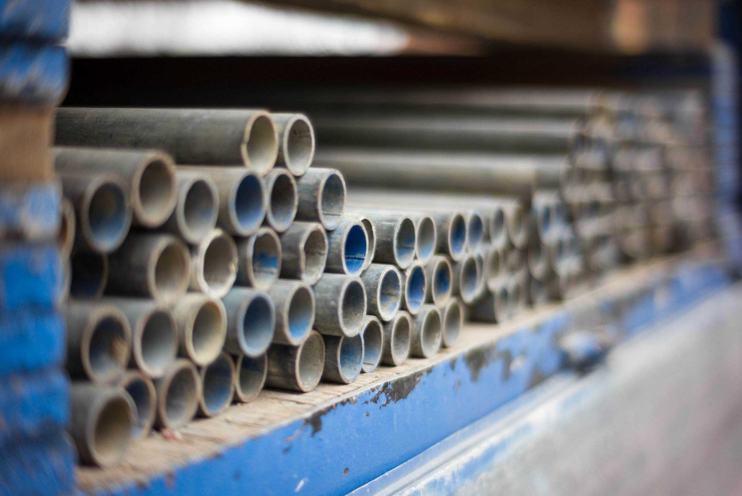 Close-up of stacked metal pipes with a blue and brown background.