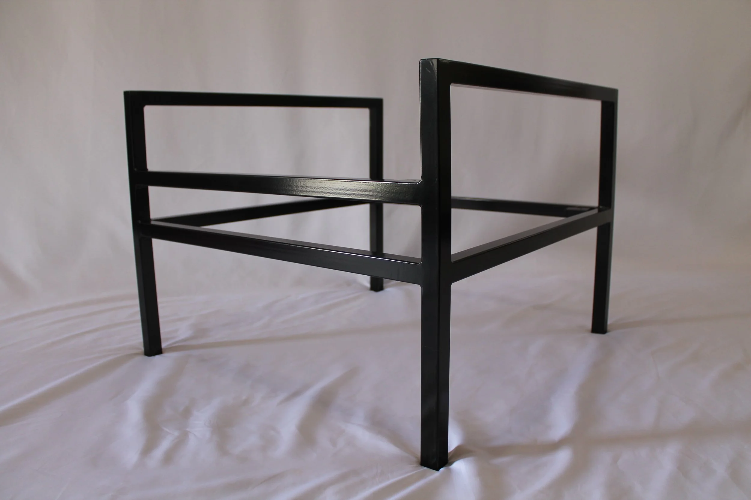 A minimalist black metal frame of a chair or table with clean lines, placed on a white backdrop.