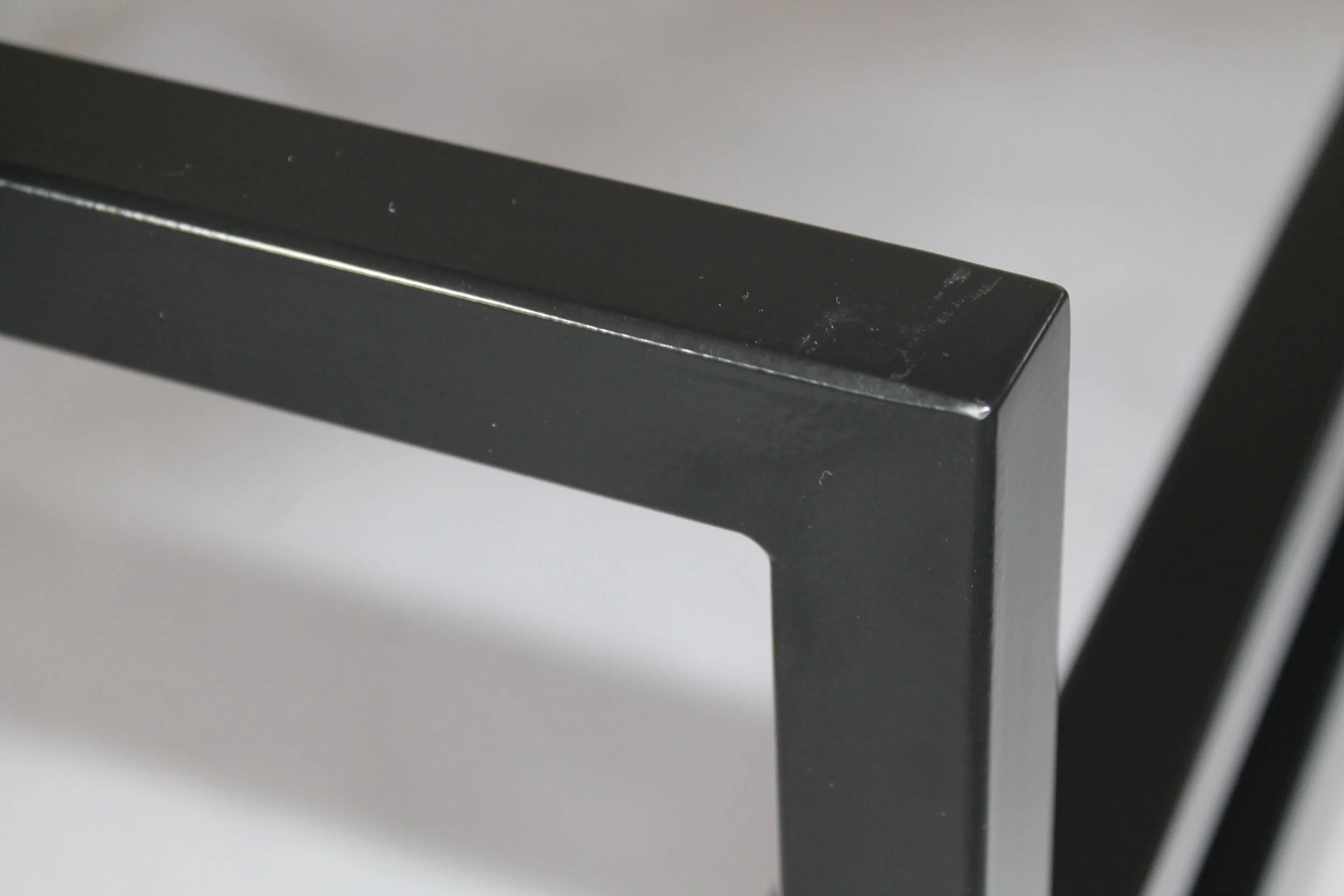 Corner of black metal chair, with a white surface in the background
