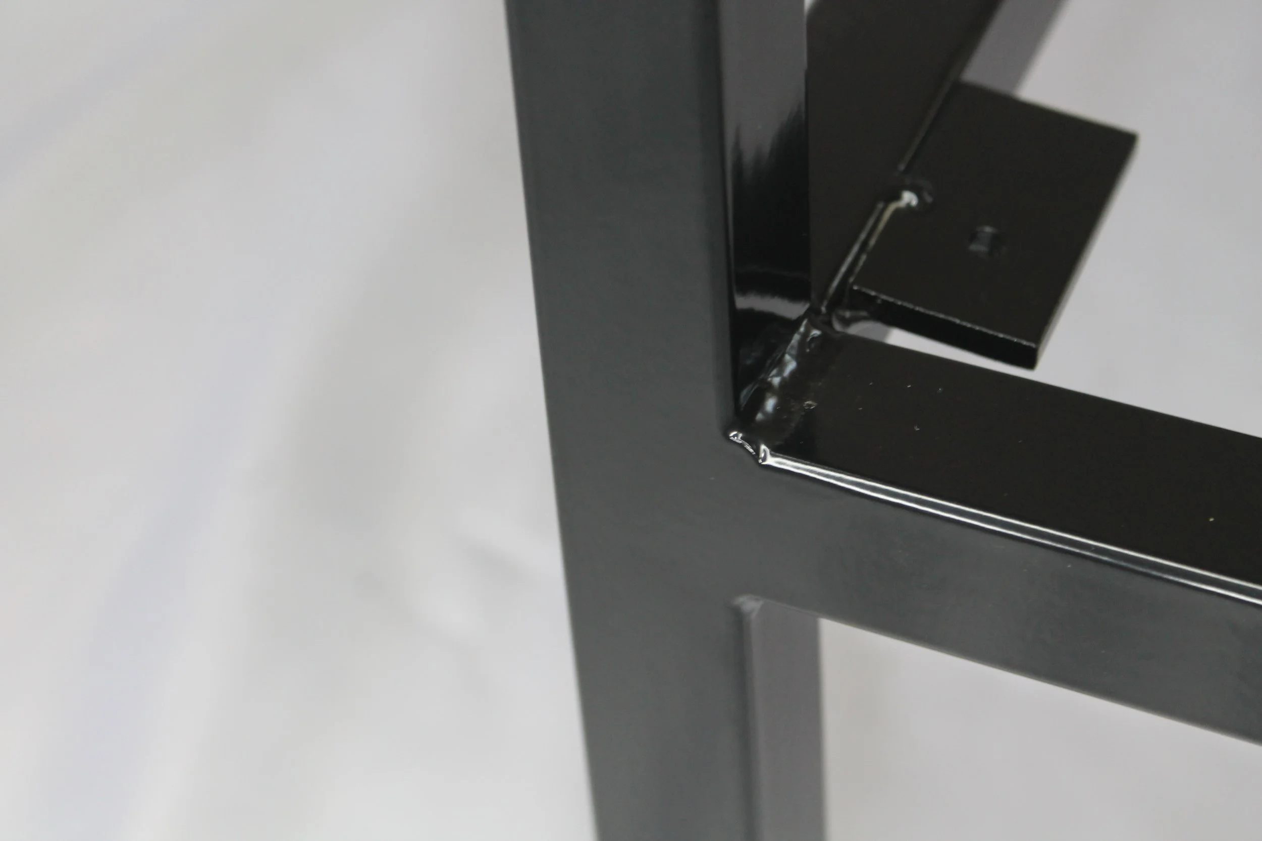 Inside corner of black metal chair, with a white surface in the background