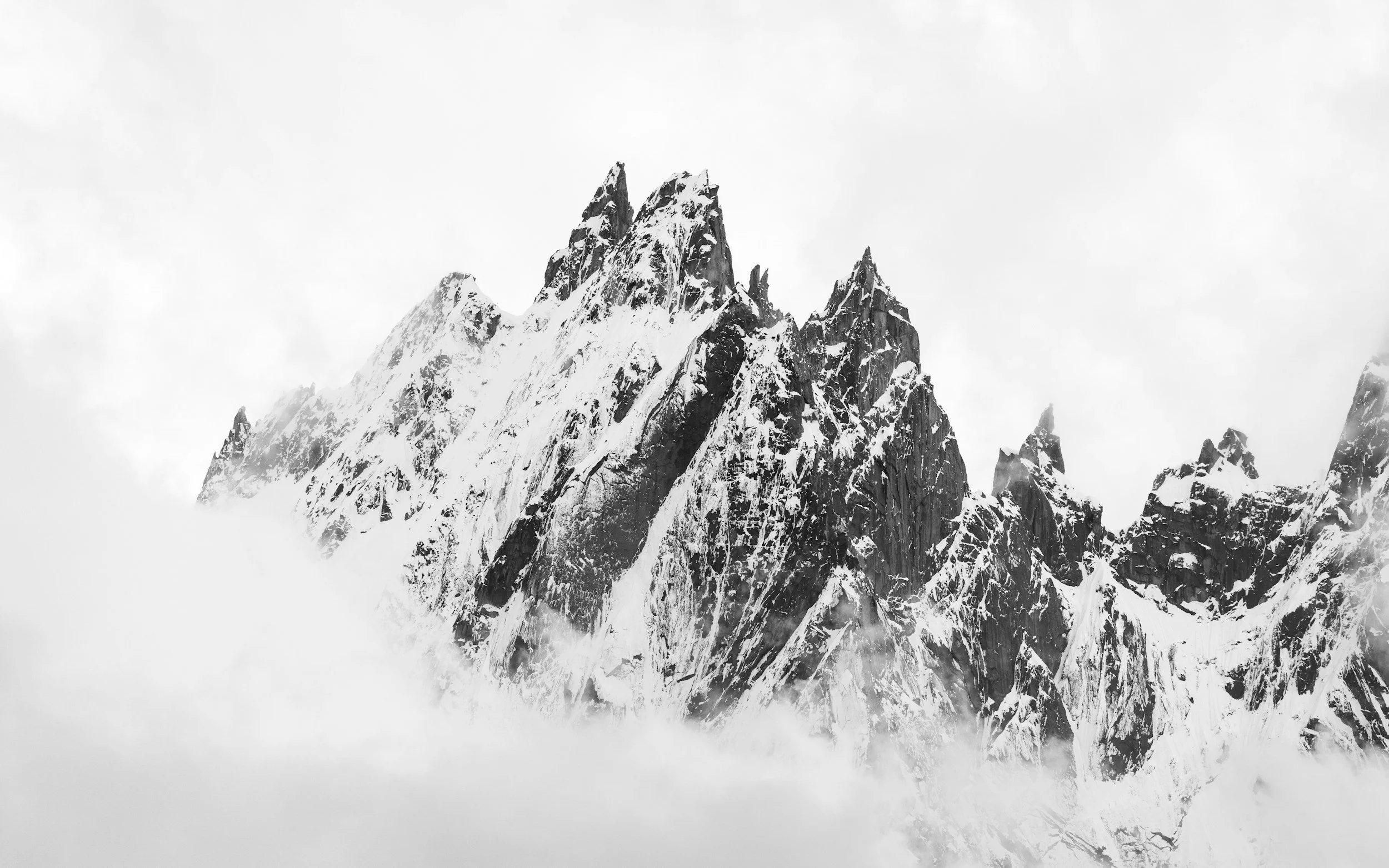 Snow-covered mountain peaks under a cloudy sky in black and white.
