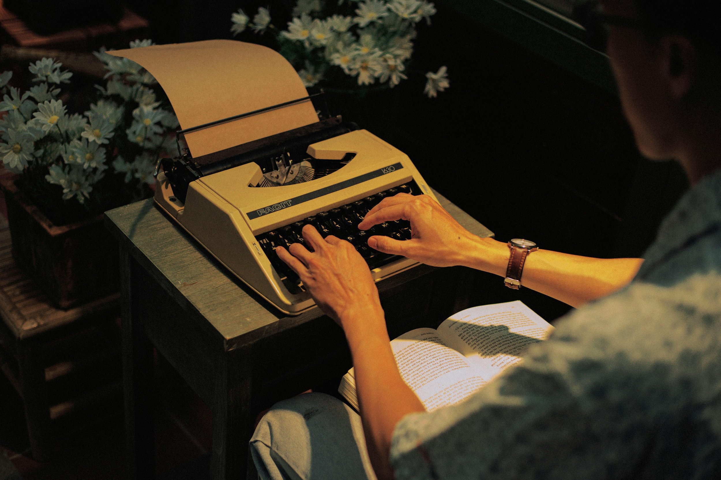 Person typing on typewriter with a book in their lap
