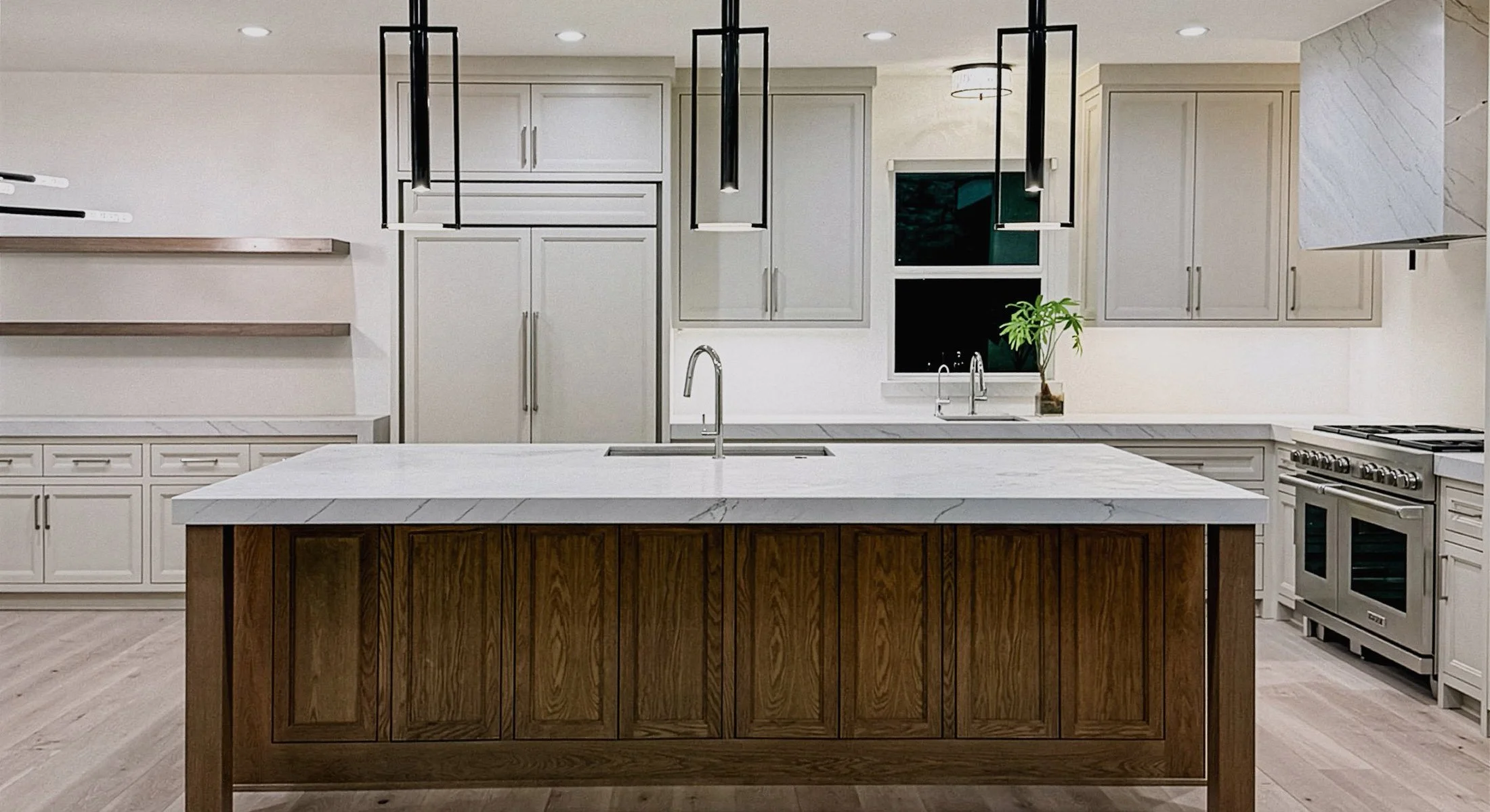 Modern luxury kitchen remodel with warm white cabinets, a dark kitchen island, black pendant lights, and professional level appliances.