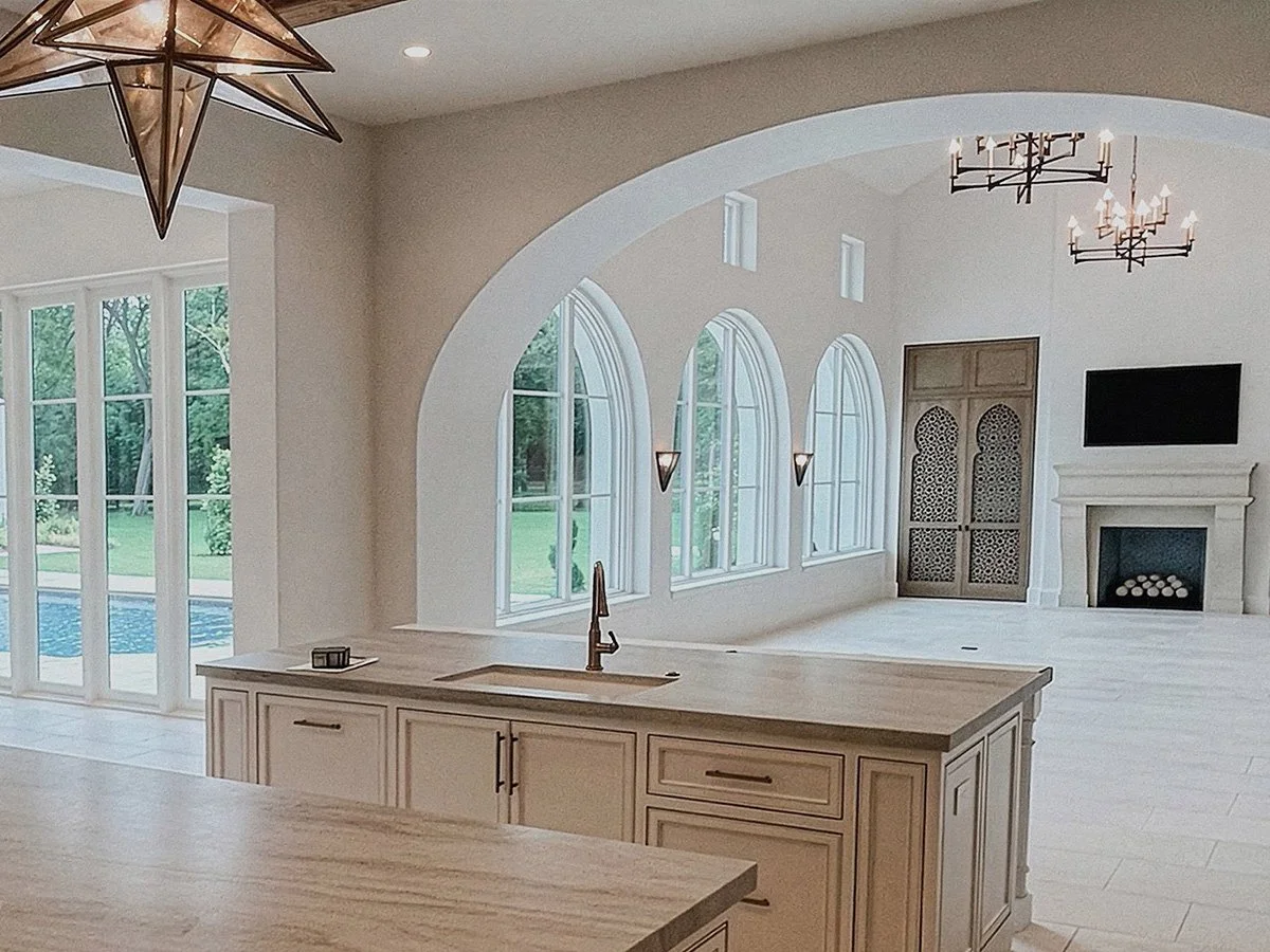 Spacious living room with large arched windows, a fireplace, glass star pendants, open kitchen area, and artistically carved, custom wood cabinetry.