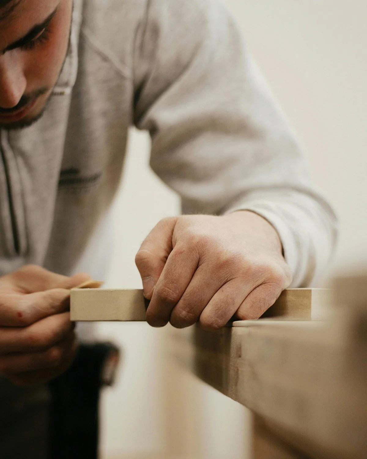 A man in a light gray sweatshirt using a tool to work on a piece of wood.