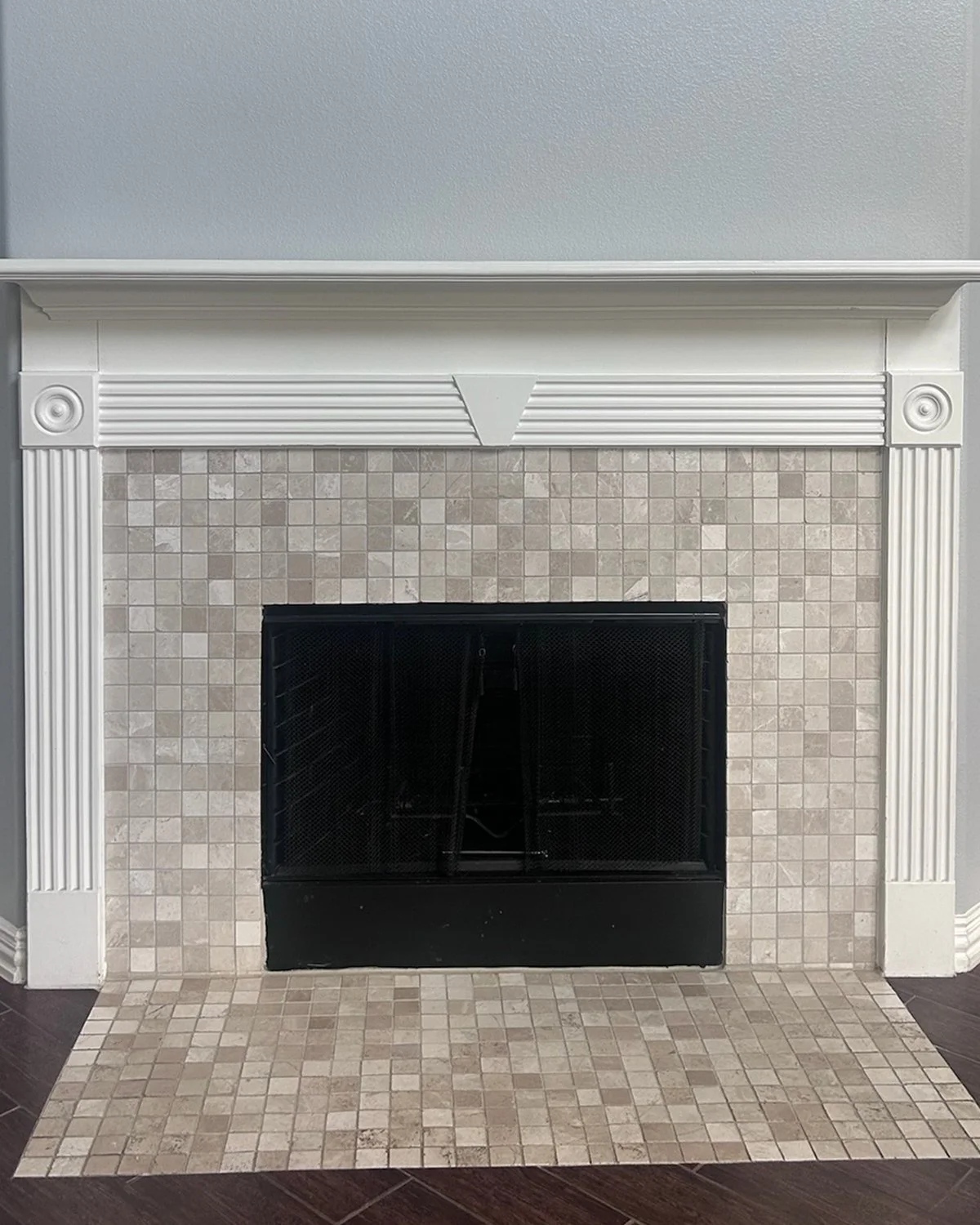 A dated fireplace with white mantel, beige tile surround, and black grate.