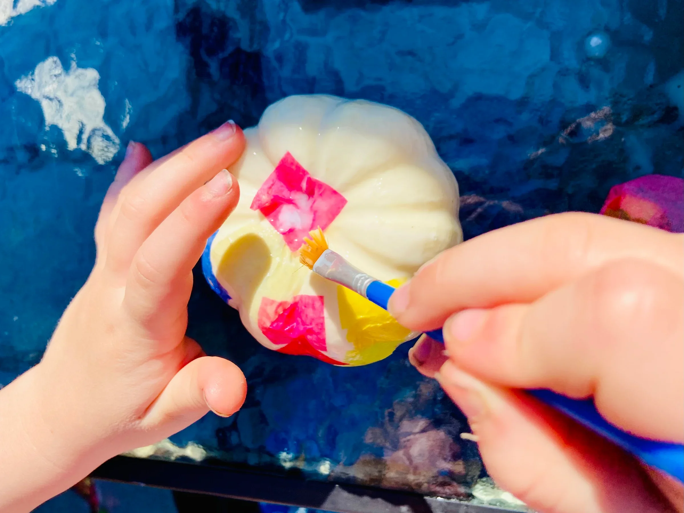 Child holding a white pumpkin with a red sticker, using a syringe.