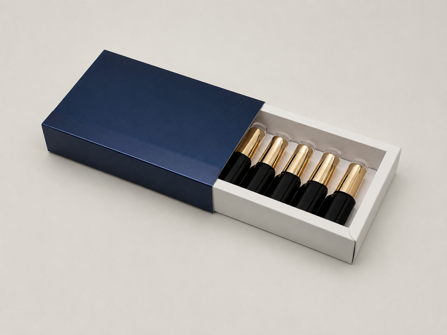 A dark blue box with a white interior containing six black bottles with gold caps.