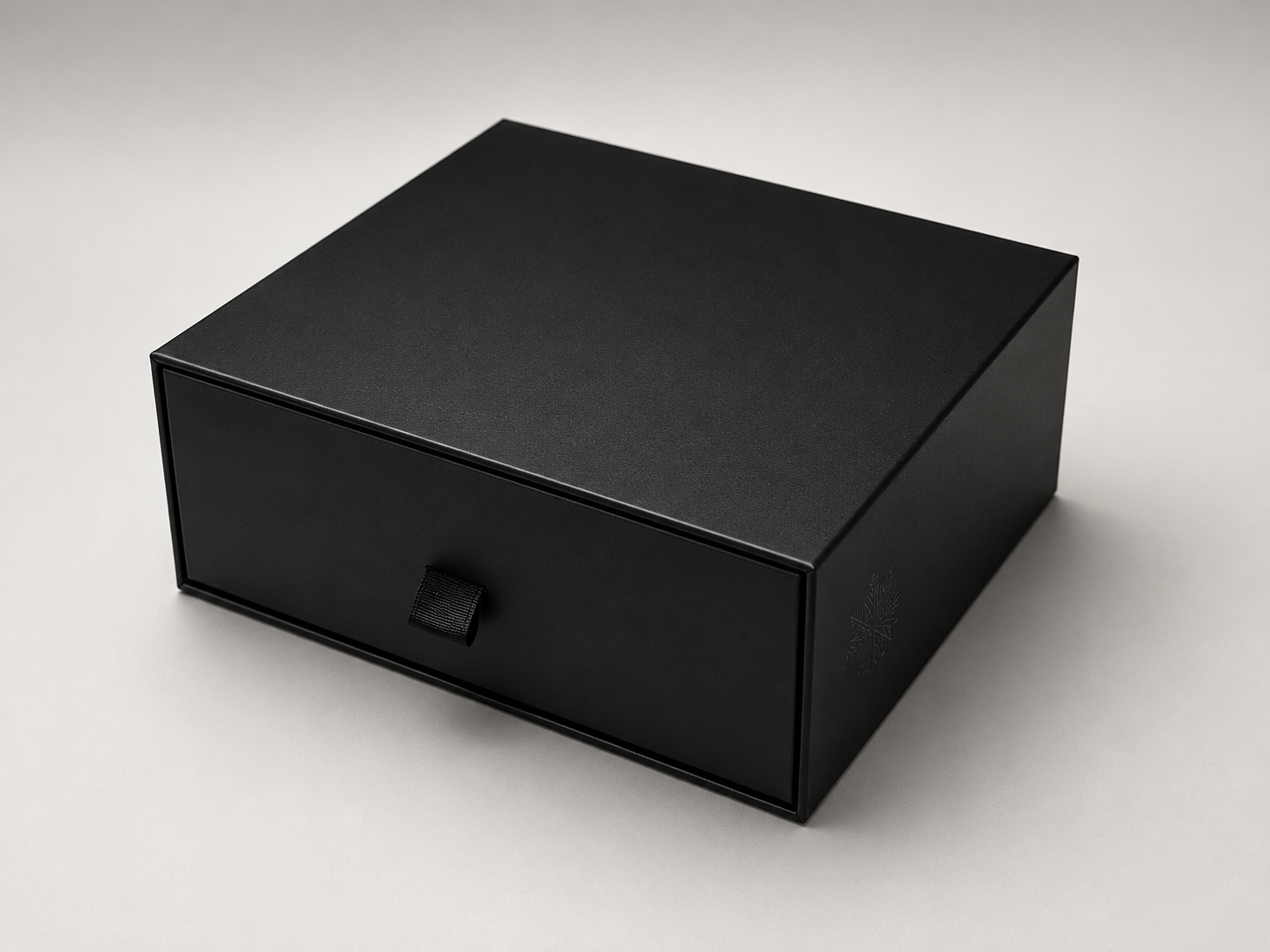 Black box with a small handle on the front, placed on a white surface, with a subtle logo on the side.