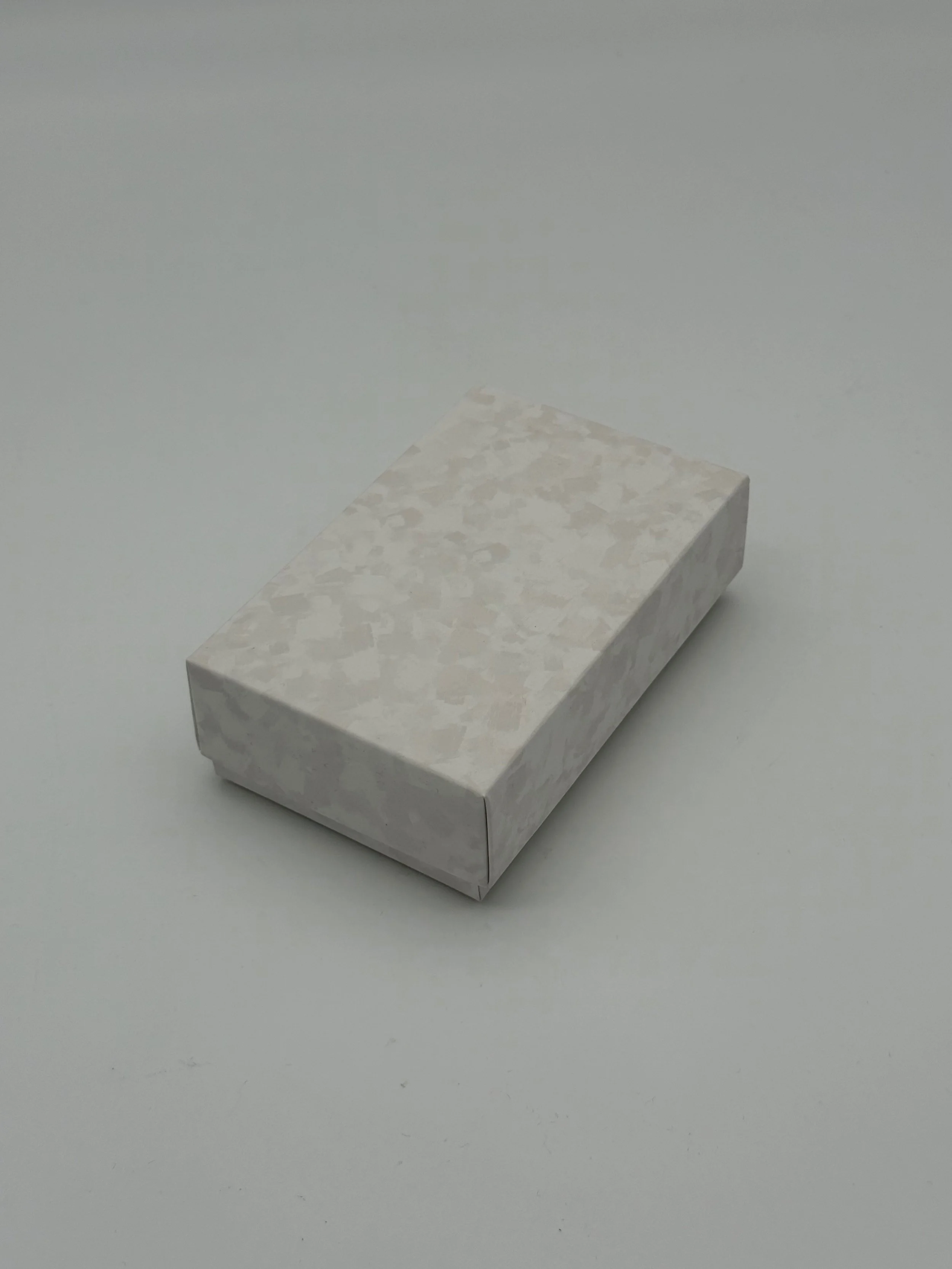 A rectangular block with a white and beige marbled pattern, placed on a plain light gray surface.