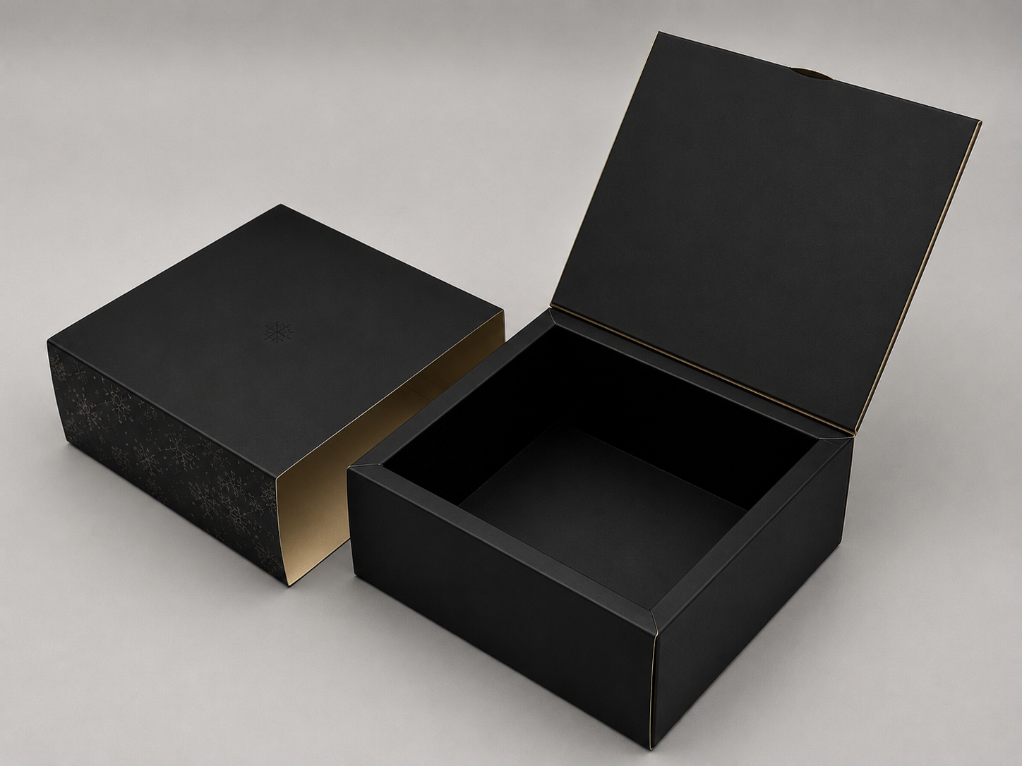 Black gift box with gold snowflake patterns and an open black lid, empty inside, on a light gray surface.