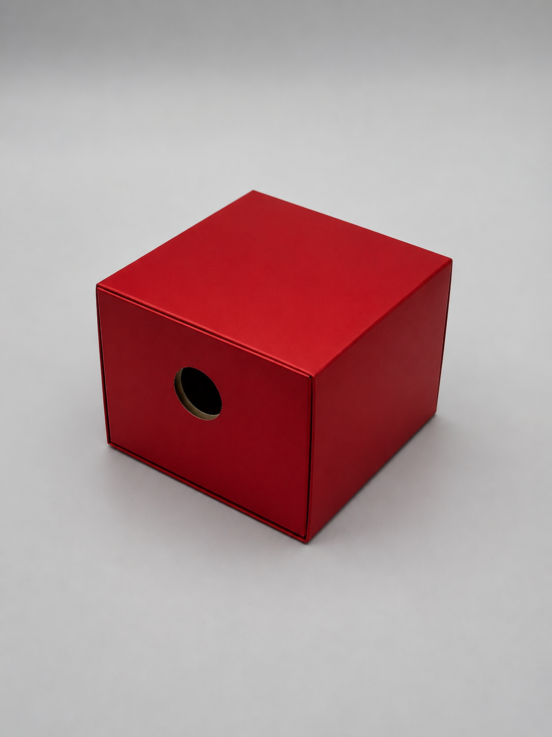 Red cardboard box with a circular hole in the front, placed on a light gray background.