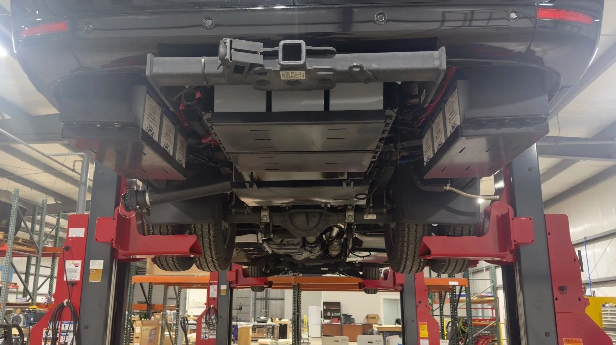 The underside of a vehicle lifted on a hydraulic lift in a workshop or garage.
