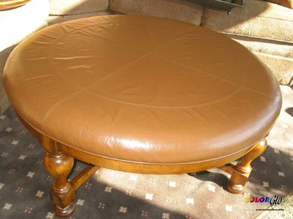 Round wooden table with a brown leather top, supported by four carved wooden legs.