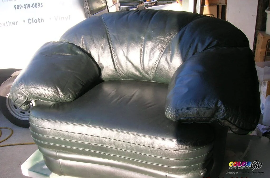 Black leather loveseat with overstuffed arms in a garage or storage area.