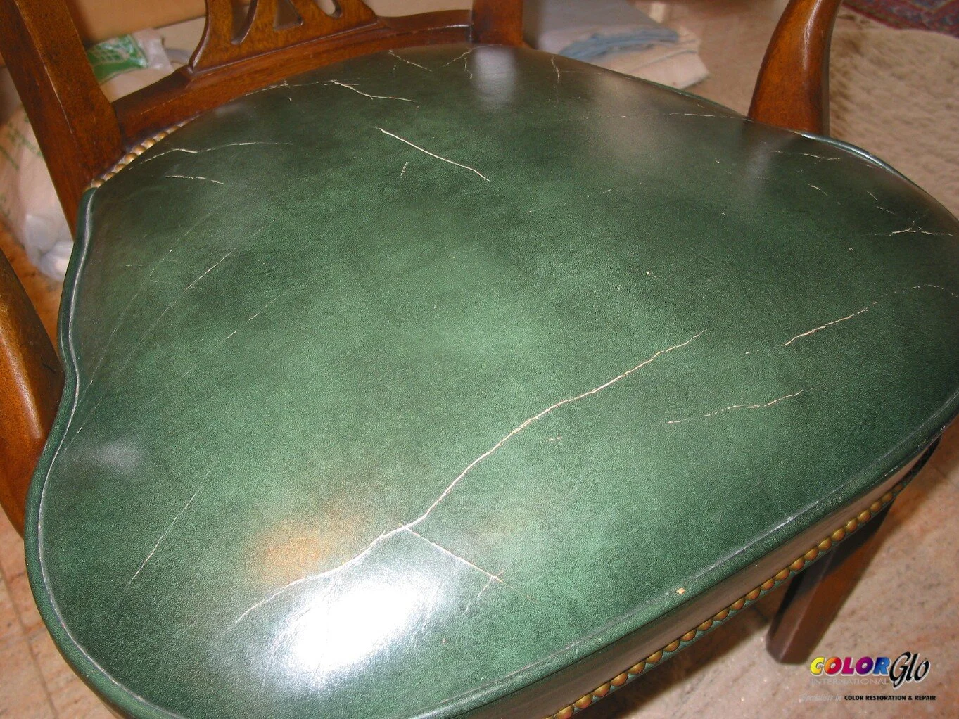 Close-up of a worn, cracked green leather chair seat with scratches.
