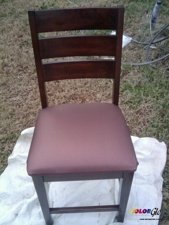 A wooden chair with a padded seat, placed on a white fabric outdoors on grass.