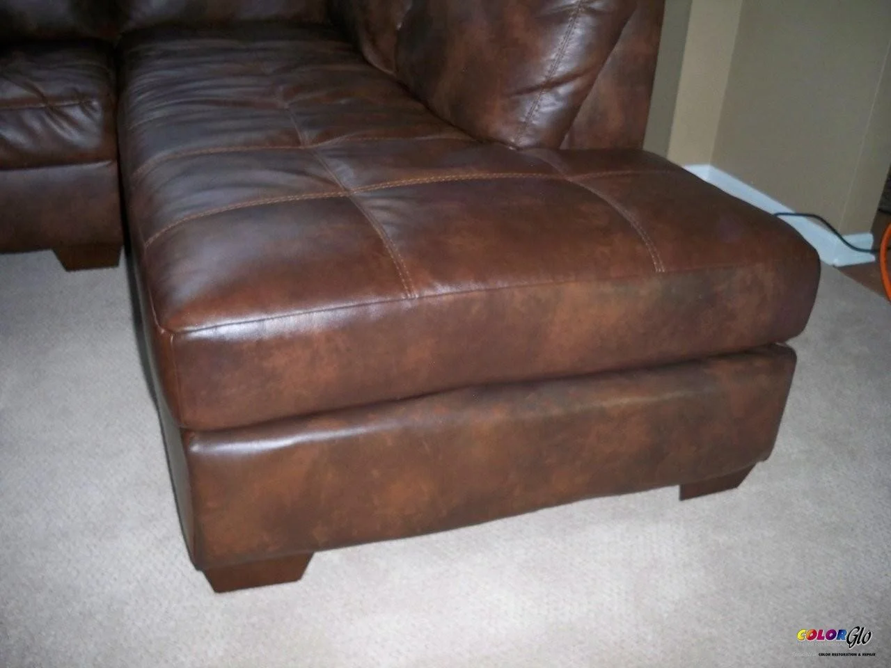 Brown leather ottoman with stitched pattern on a beige carpet.