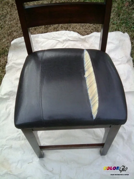 A wooden chair with a black leather seat that is partially removed, revealing yellow foam underneath.