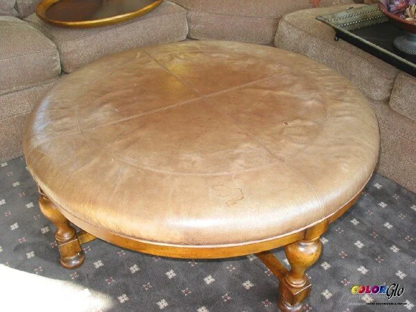 Round wooden coffee table with a leather top, sitting on a patterned carpet in a living room.