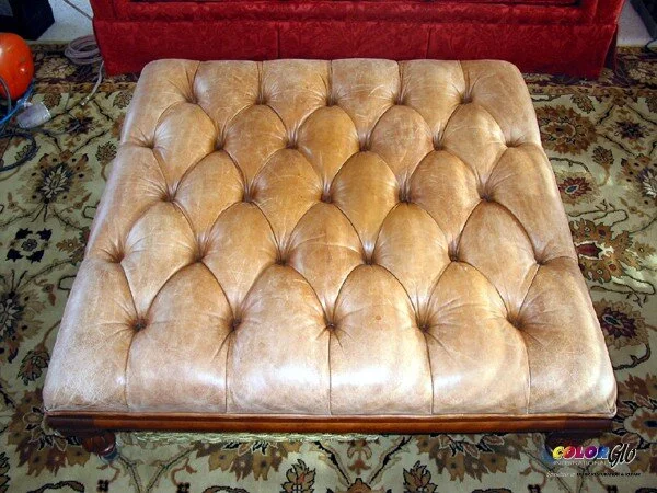 Button-tufted, tan-colored upholstered ottoman or bench on a floral patterned rug.