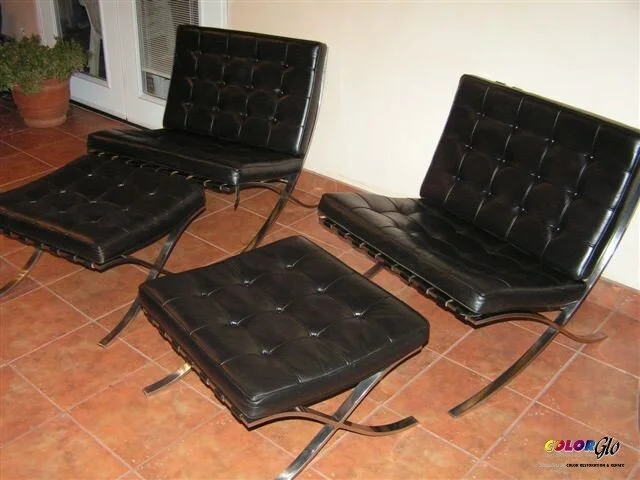 Three black leather lounge chairs with matching ottomans arranged on a tiled floor inside a room.