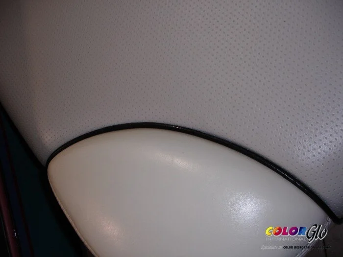 Close-up of the seat and backrest of a white leather or vinyl barber or salon chair with black trim.