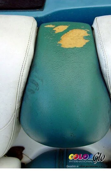 Close-up of a worn, teal-colored seat with peeling yellowish-green material on top, situated between two white seats.