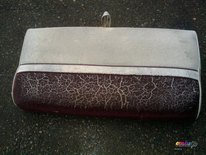 A worn-out, cracked car stereo or speaker with a silver and black design, placed on a gravel surface.