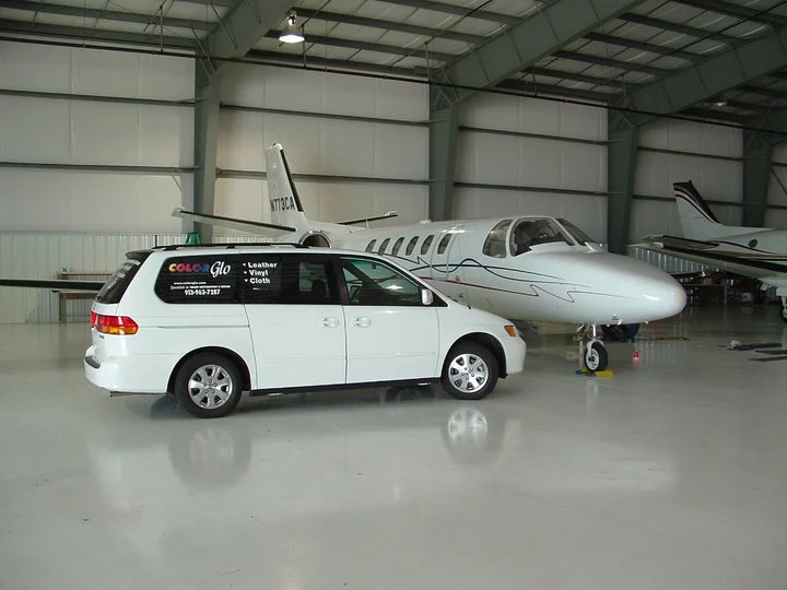 A white van parked inside an airplane hangar with a private jet behind it.