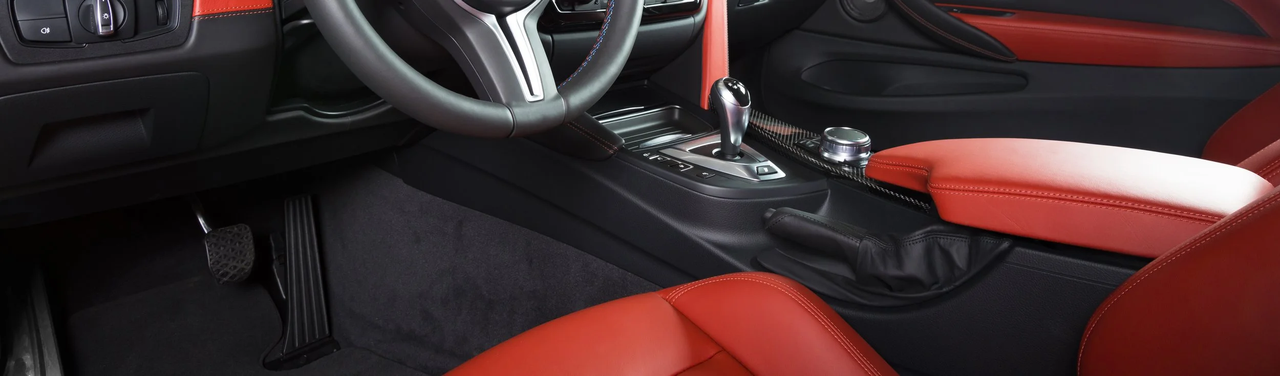 Interior of a modern car showing the steering wheel, center console with gear shift, and red leather seats.