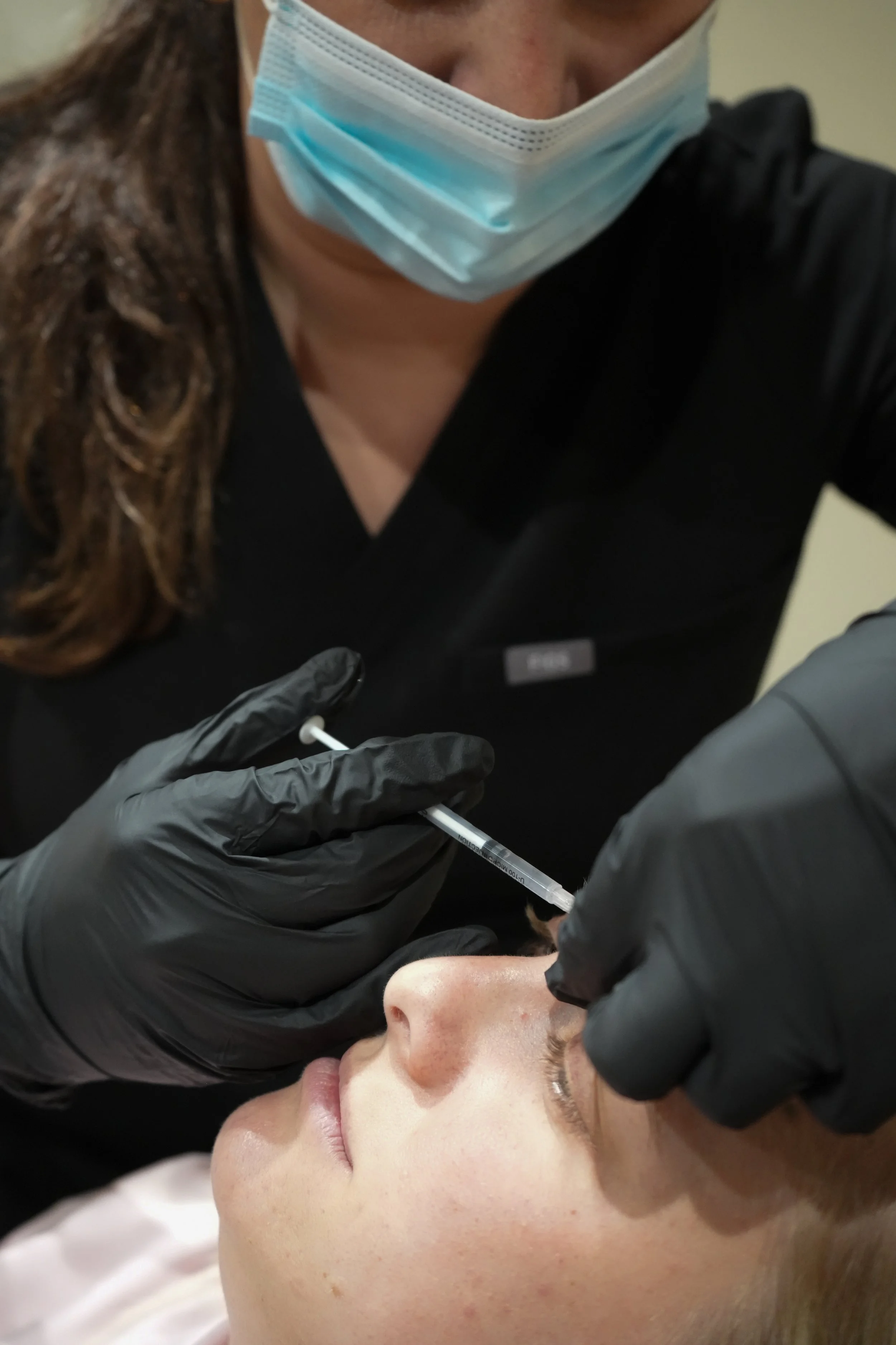 A person receiving a vaccination or injection from a healthcare professional with gloved hands, while the person is lying down.