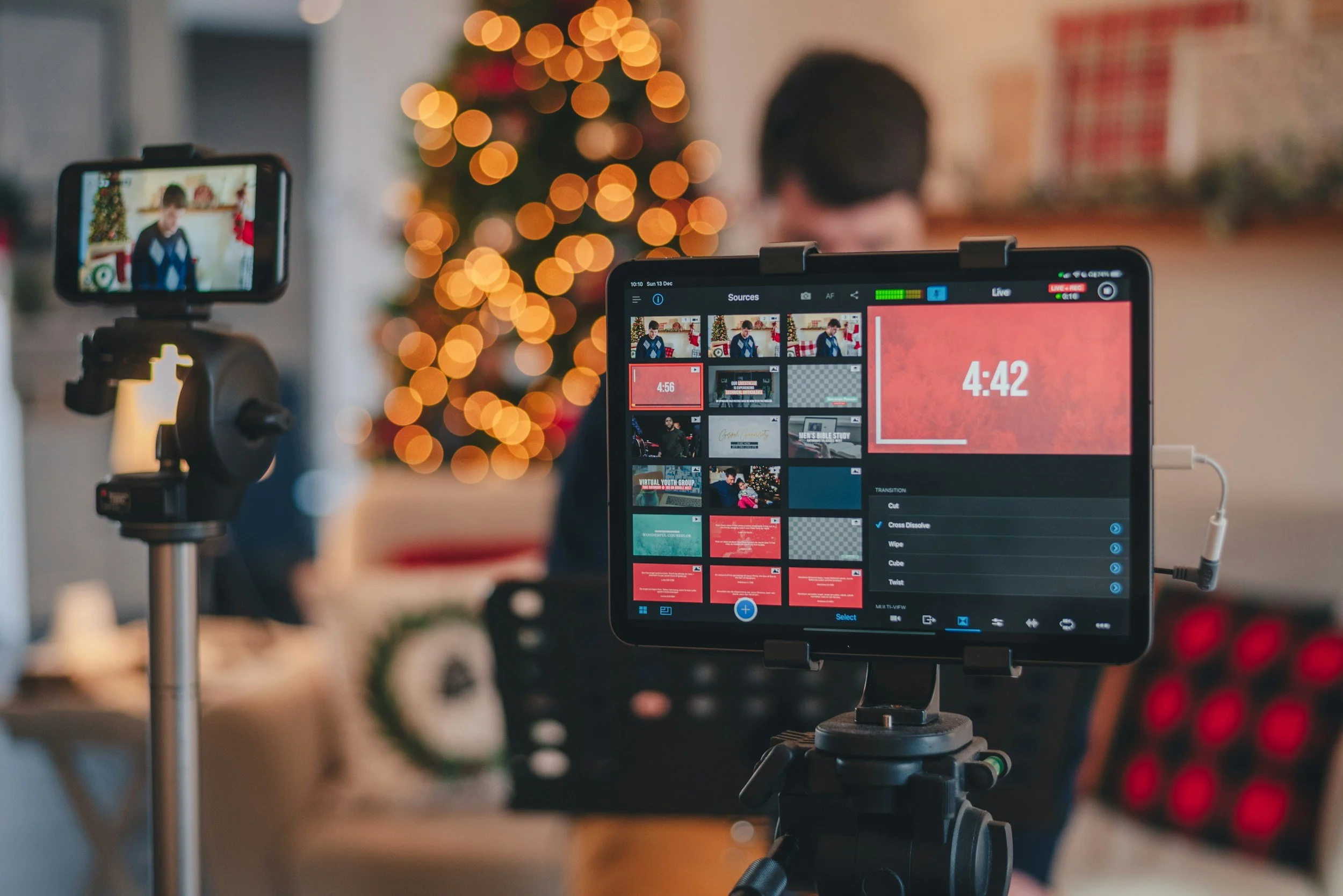 Video camera and monitor recording a person in front of a decorated Christmas tree with colorful lights.