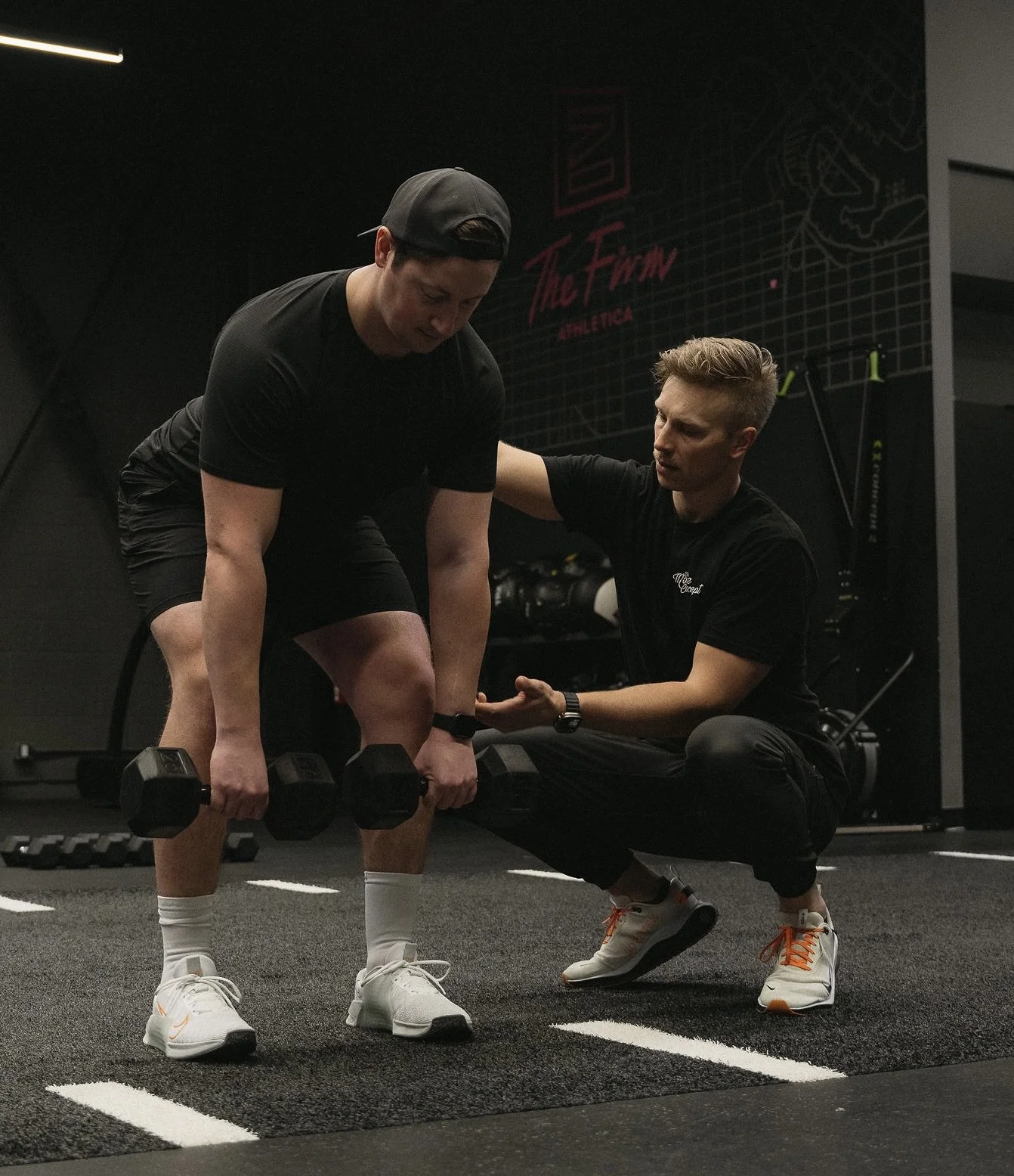 A personal trainer assisting a man with a weightlifting exercise in a gym.
