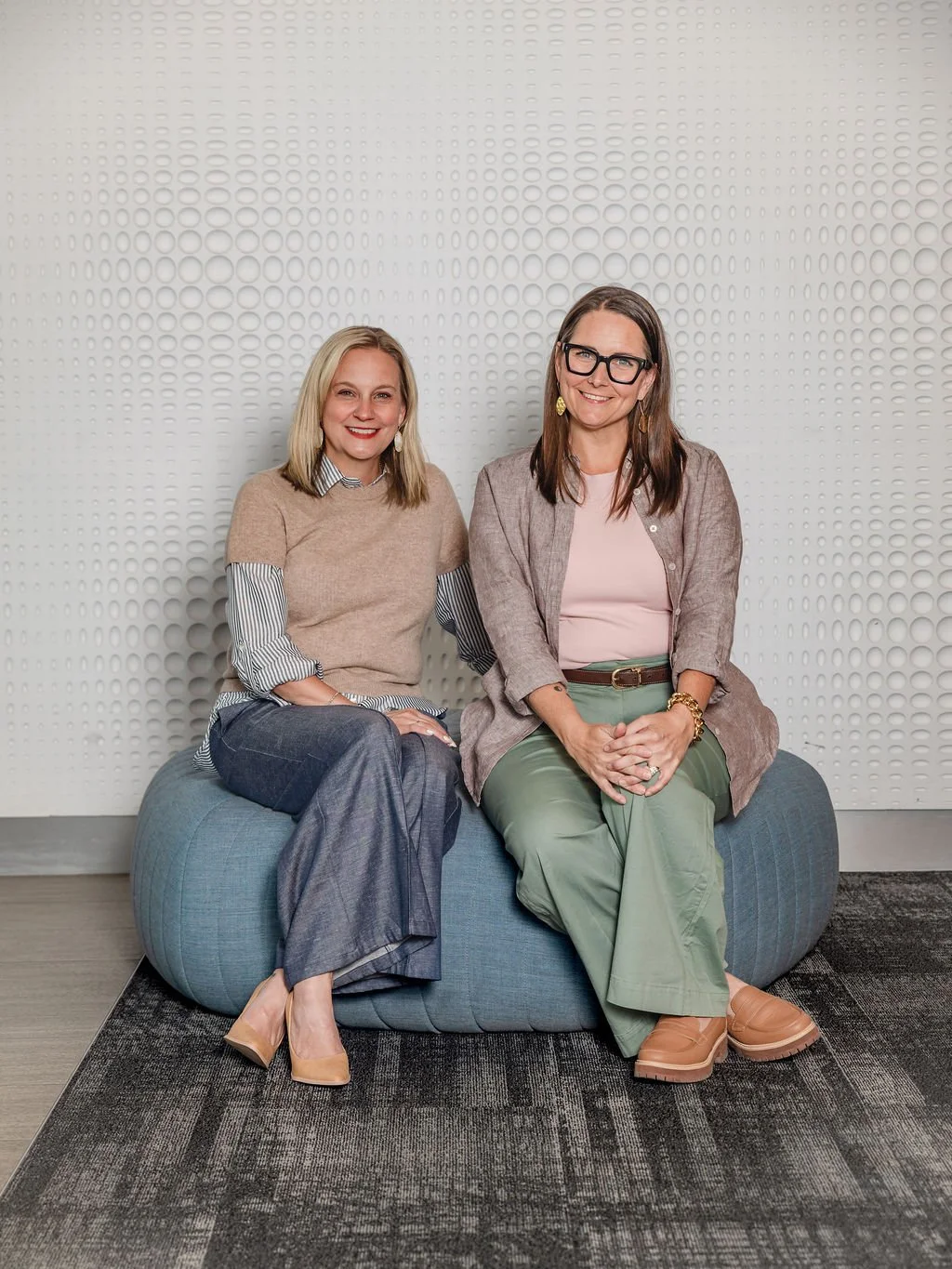 Rooted Hire team members Brittny Wilson and Courtney Schwartz sitting together on a bean bag chair in an office setting