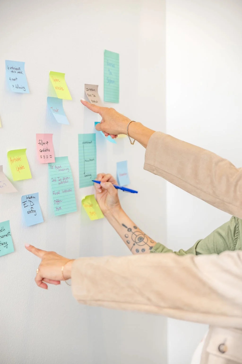 3 hands pointing at a wall filled with stickynotes