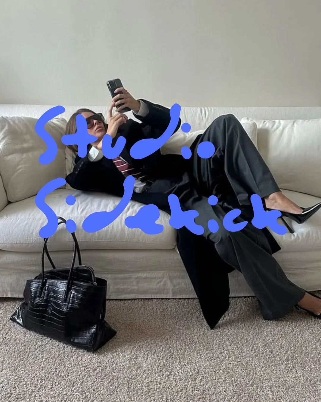 Person lying on a white sofa, wearing sunglasses and a black suit, taking a selfie with a phone. Handwritten blue text says 'Stupid' and 'Sketch' across the image. A black handbag is on the floor nearby.