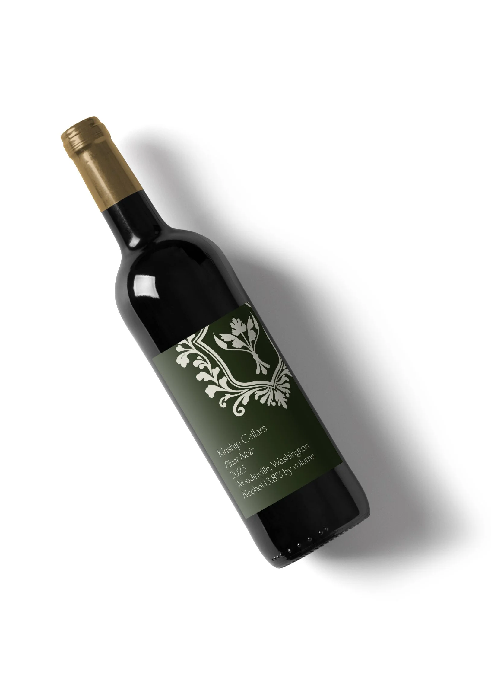 A bottle of Kinship Cellars Pinot Noir wine with a dark green label and gold foil on the neck, placed against a white background.