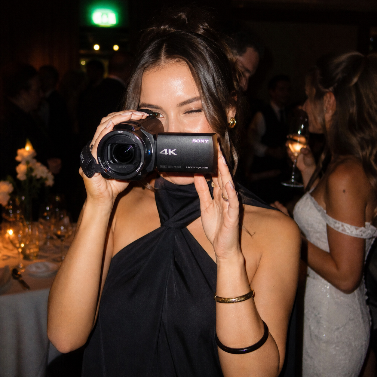 Woman with dark hair in an elegant black dress filming with a 4k camcorder rental at a formal event.