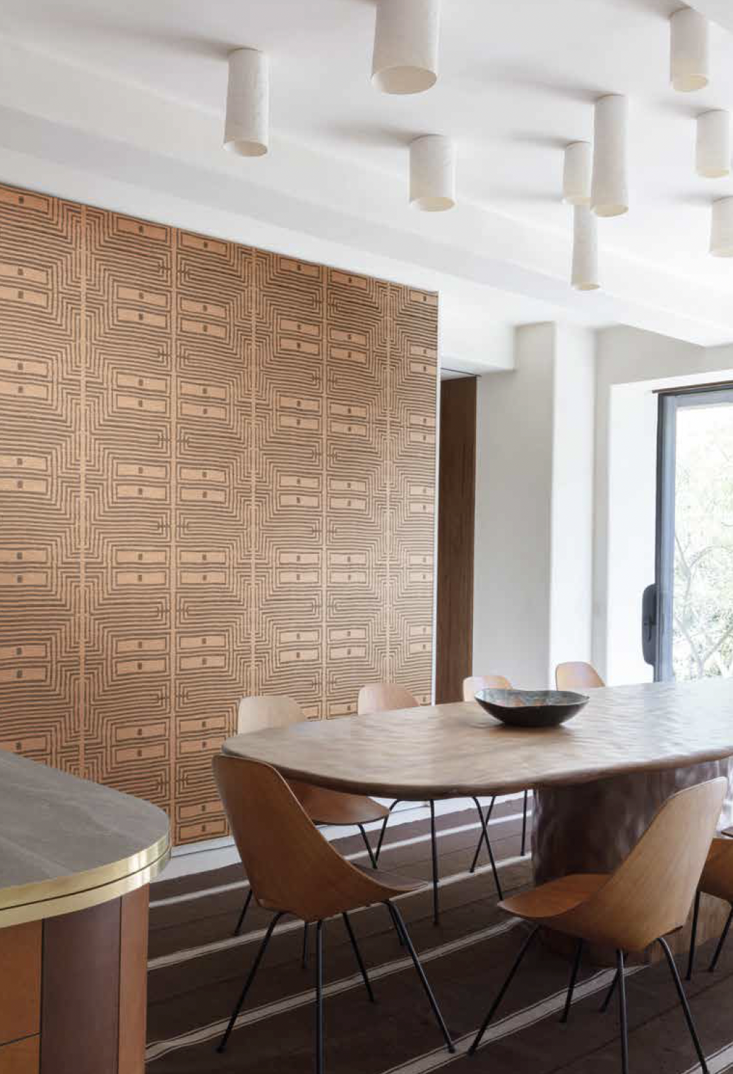 Moderne eetkamer met houten tafel en stoelen, decoratieve houten wand en witte plafondverlichting.