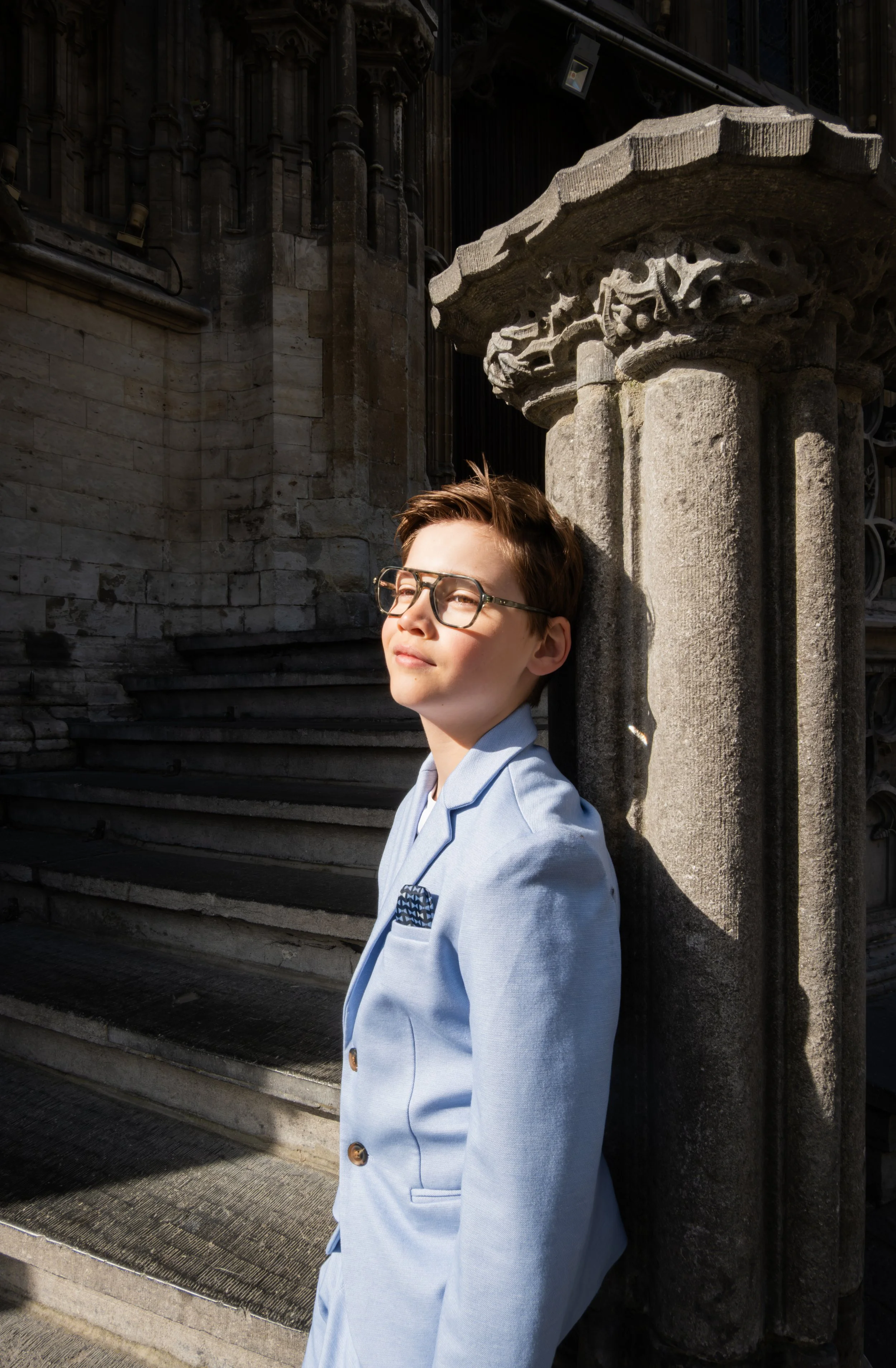 Professioneel portret van een communicant in een lichtblauwe blazer bij een historisch gebouw.