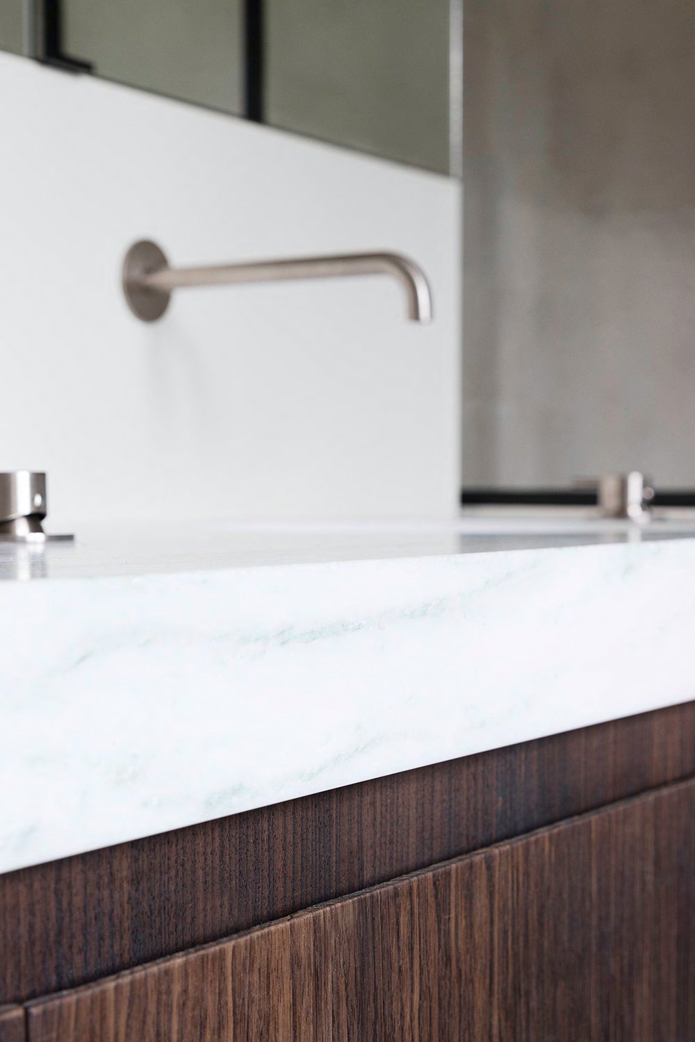 Interieurdetail van een moderne badkamer met witte marmeren wastafel en donker houten meubel.