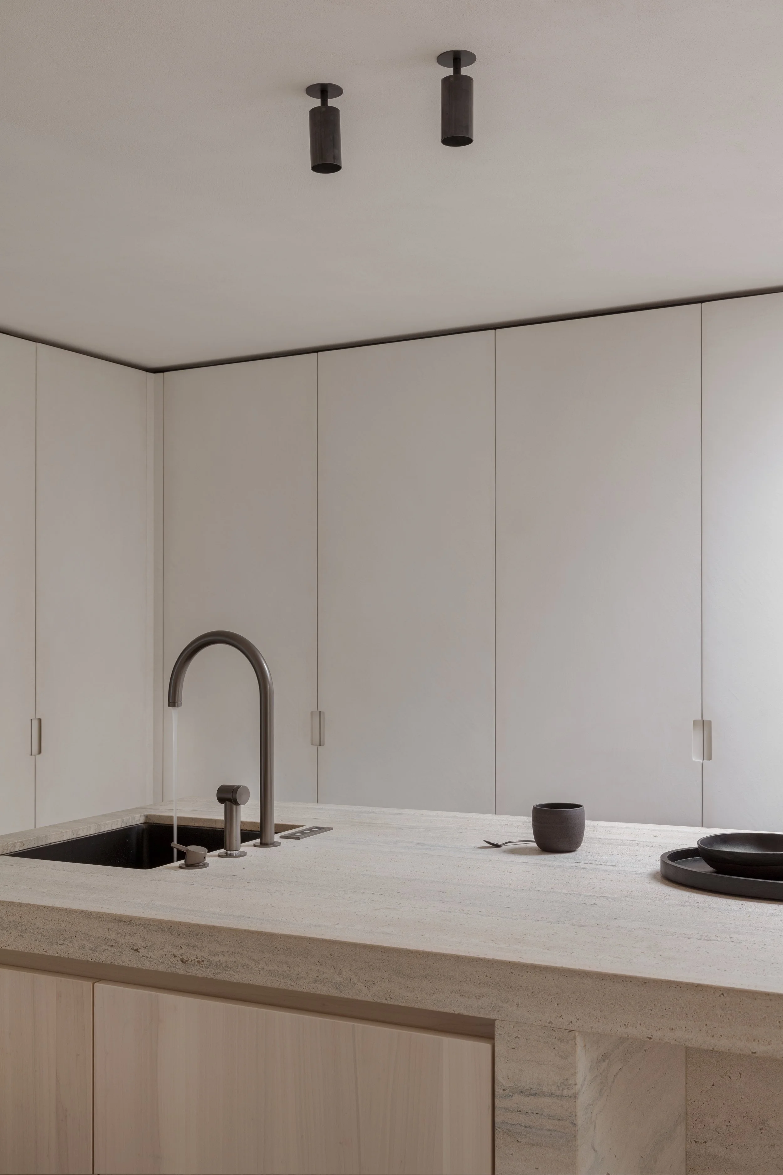 Moderne keuken met beige kasten, wit werkblad, zwarte spoelbak en donkere hanglampen.