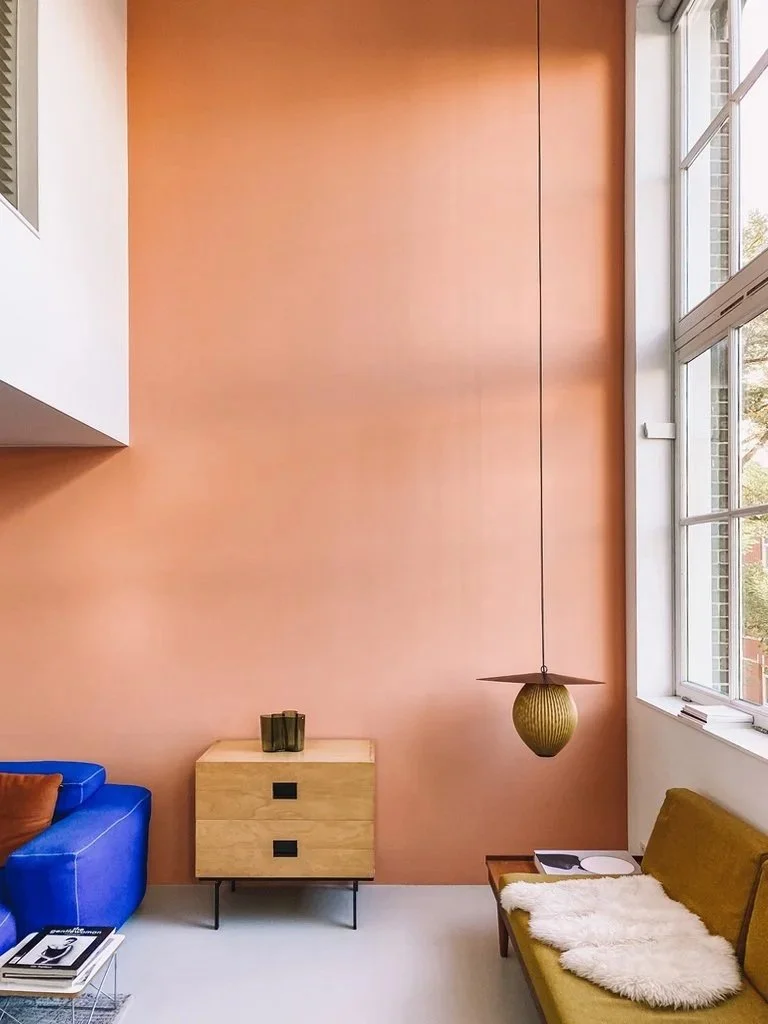 Interieurfotografie van een kleurrijke woonkamer met roze wand, blauwe zetel en gele fauteuil.