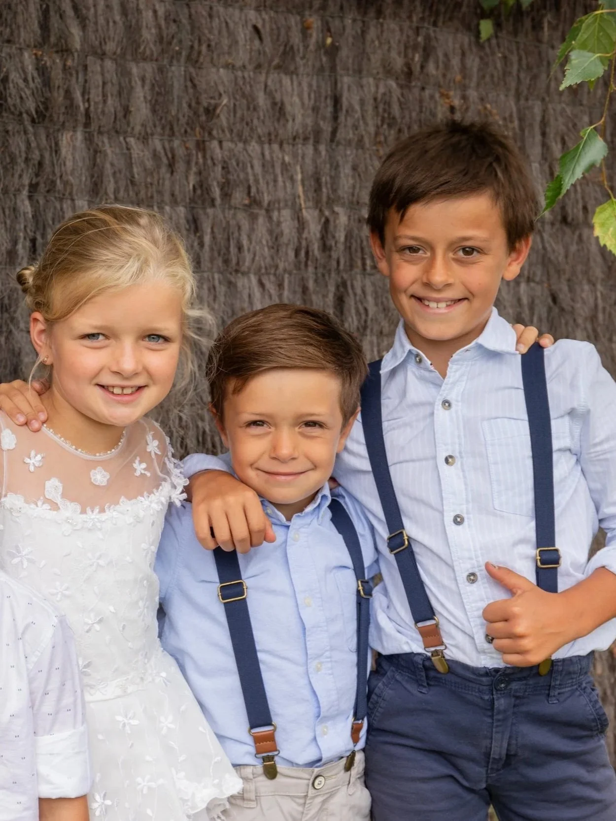 Drie lachende kinderen poseren samen bij een boom tijdens een familiefeest.