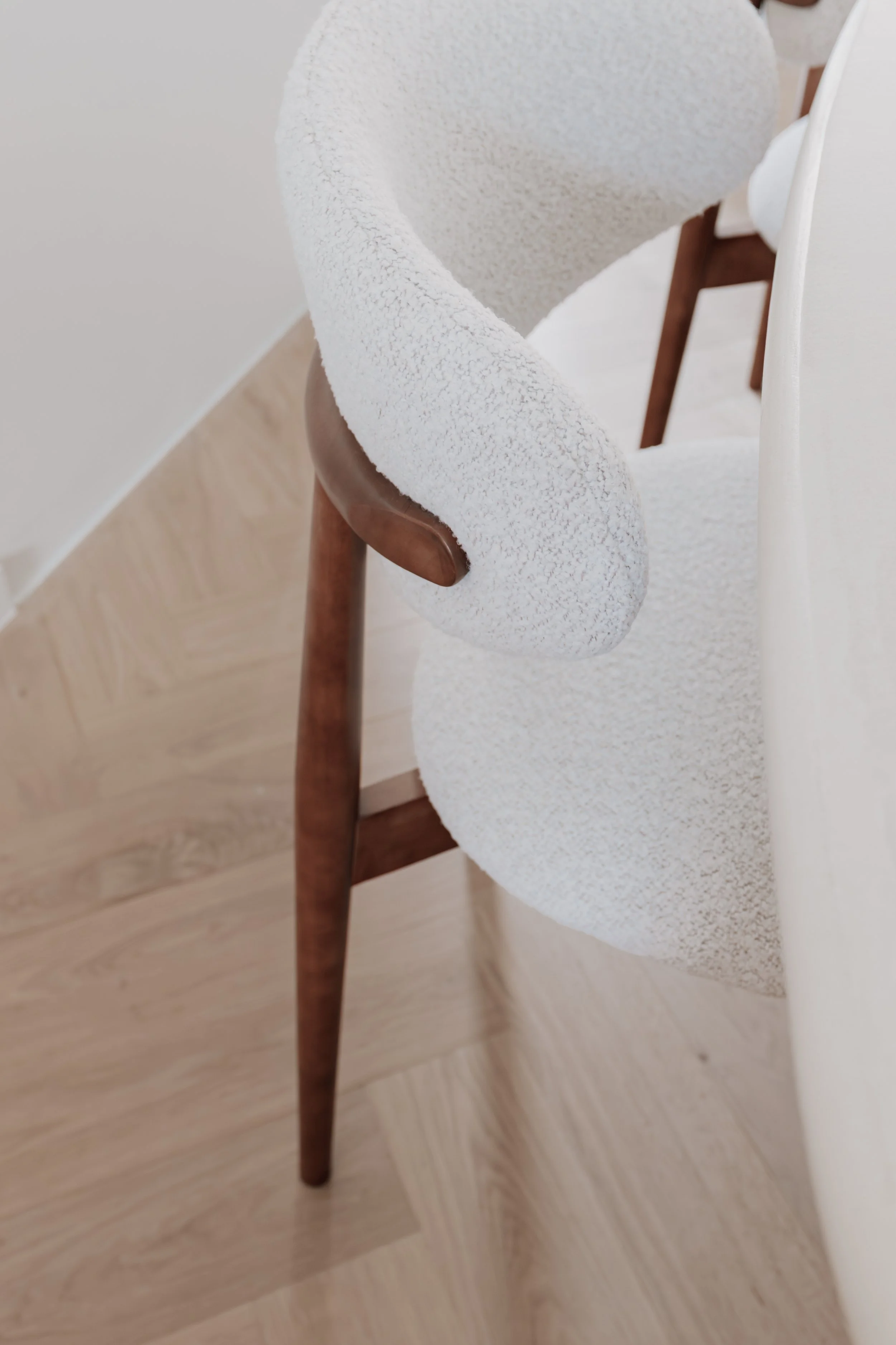 Detailfoto van een houten stoel met gebogen rugleuning en zachte witte bekleding.