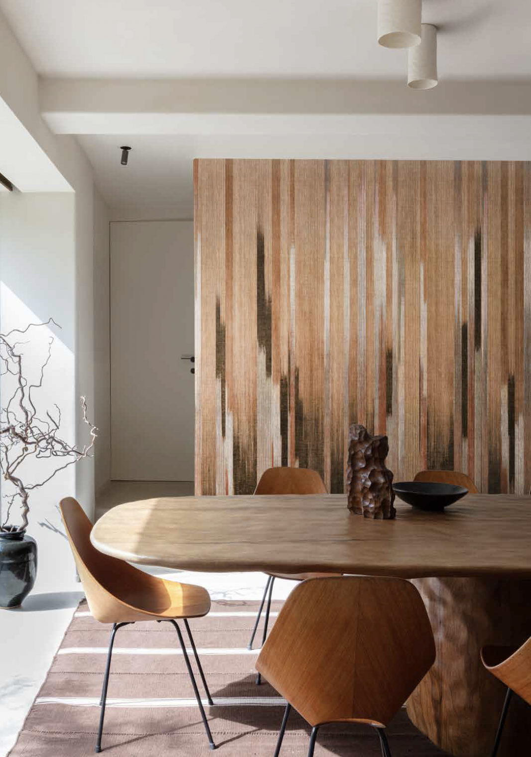 Warme eetkamer met houten tafel, oranje stoelen, houten accentwand en sculpturale decoratie.